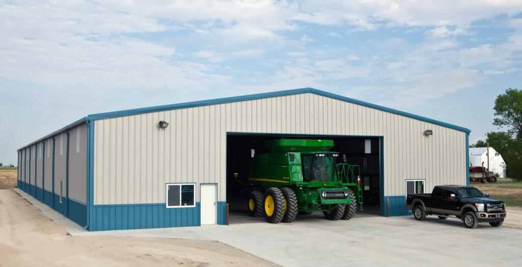 Large beige ag building with blue wainscoting and a green combine parked inside the open bay.