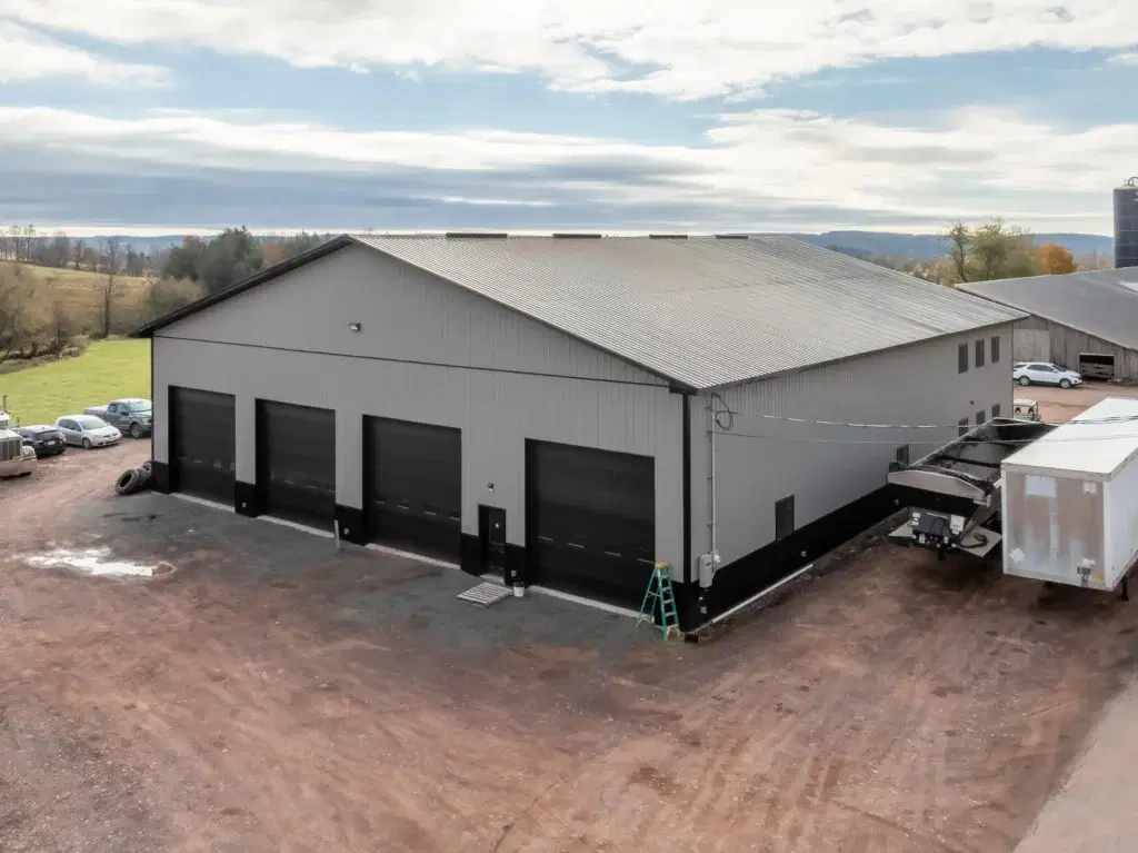 Large grey post-frame commercial warehouse featuring multiple black garage bays and heavy-duty metal siding.