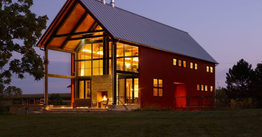 Modern white barndominium with a black metal roof and wooden porch pillars.