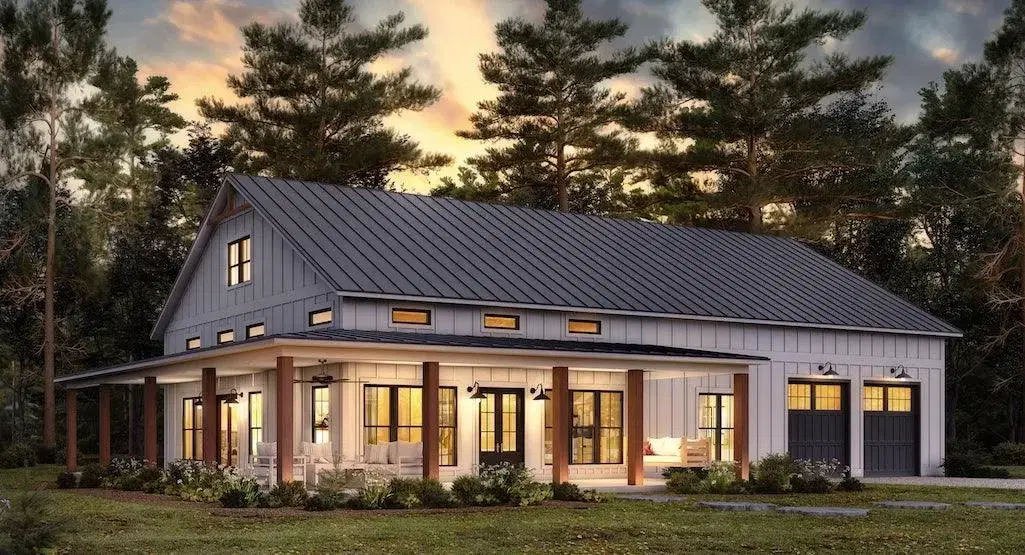 Modern white barndominium with a black metal roof, wooden porch pillars, and an attached garage.